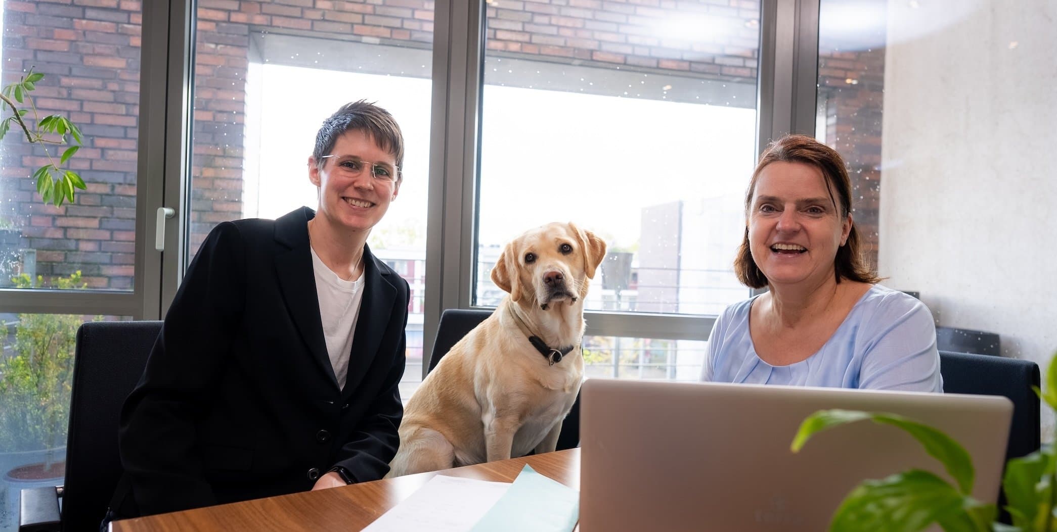 Helga Habrock, eine Mitarbeiterin und ein Hund am Schreibtisch